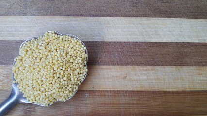 millet grains on a large metal spoon placed on a kitchen Board, vegetarian healthy food, space to copy the text