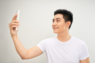 Smiling young asian man making selfie photo on smartphone over white background