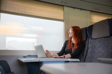 A ginger woman sitting in the train and working with a laptop - looking in the window