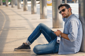 male business executive sitting on pathway outdoor and using smartphone