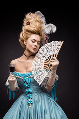 attractive victorian woman holding fan and wine glass while standing on black