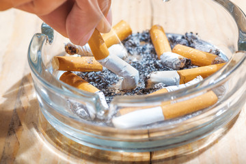 Hand stubbed out cigarette in a transparent ashtray