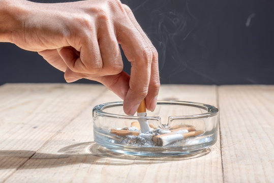 Hand stubbed out cigarette in a transparent ashtray