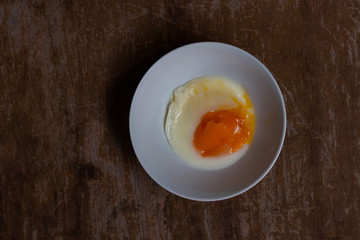 Soft-boiled egg in small white bowl on wooden table.