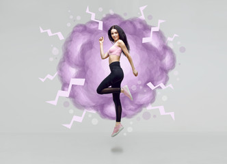 Amazing woman in trendy sportswear jumping. Smiling beautiful slim brunette young girl in fashion leggings and pink top expressing happy emotions. Gray background.