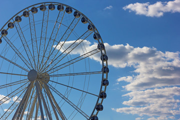 Ferris of National Harbor against cloudy skies in Oxon Hill, Maryland, USA. Sun shines through cumulus clouds on the Ferris.