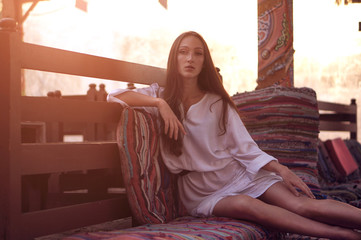 Young fashion eastern woman in white dress relaxing in traditional oriental interior in arabic town.