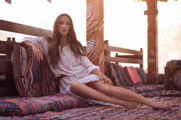 Young fashion eastern woman in white dress relaxing in traditional oriental interior in arabic town.