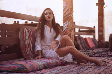 Young fashion eastern woman in white dress relaxing in traditional oriental interior in arabic town.