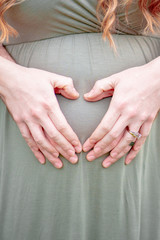 Closeup Of Heart Shape Of A Couple Hands Together On Pregnant Woman's Belly
