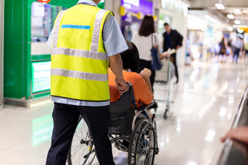 Caretaker push elderly woman on wheelchair in airport terminal.
