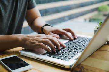 Man's hands busy working on his laptop sitting at wooden table. work and study concept.work from...