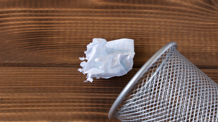 Fototapeta na wymiar Crumpled sheet of paper and metal basket. On a wooden background.