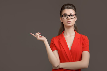Business woman pointing up at camera over gray background. Young stylish woman with glasses