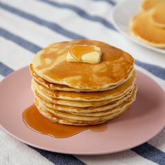 Stack of homemade pancakes with butter and maple syrup on a pink plate, low angle view. Closeup.