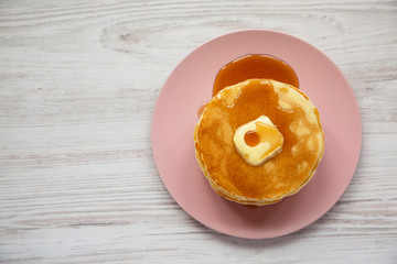 Stack of homemade pancakes with butter and maple syrup on a pink plate on a white wooden background, top view. Overhead, from above, flat lay. Copy space.