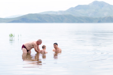 child with his grandfather and father play and swin in sea, summer time