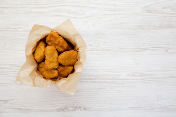 Chicken nuggets in a paper box over white wooden surface. Overhead, from above, flat lay. Copy space.