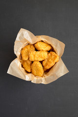 Chicken nuggets in a paper box over black background. Overhead, from above, flat lay. Close-up.