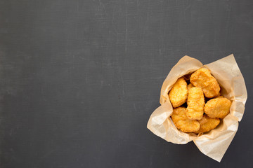 Chicken nuggets in a paper box over black surface. Overhead, from above, flat lay. Space for text.