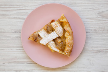 Slice of home-baked apple pie on a pink plate on a white wooden background, top view. Overhead, from above, flat lay. Close-up.