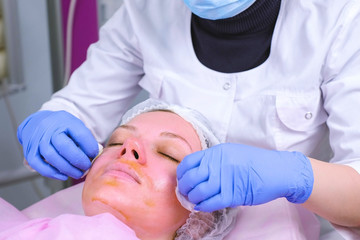 Beautician washes cotton pads chemical peeling from the patient's face.