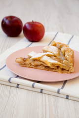 Slice of home-baked apple pie on a pink plate, side view. Close-up.