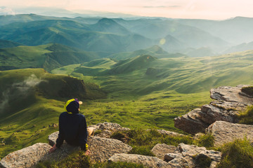 Travel man tourist sitting alone on the edge mountains over green valley adventure lifestyle extreme vacations green landscape Freedom - 276649516