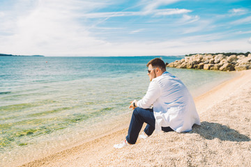 young stylish man sitting at sea beach enjoying the view