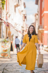 Fototapeta premium woman in yellow dress with bit straw hat walking by old tourist city in croatia