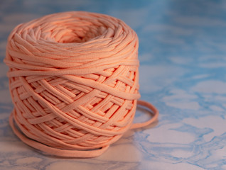 Obraz premium A coil of large knitted yarn of peach color on the surface of blue marble