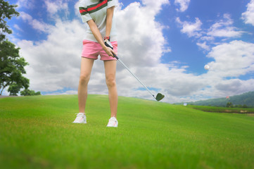 woman golf player in action hit the golf ball away from fairway to the destination green at day light sky.