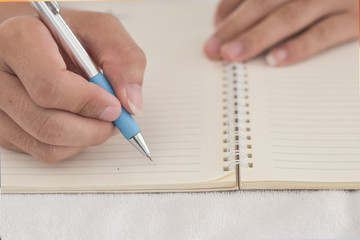 Close-up of male hand with pen writing on a notebook.