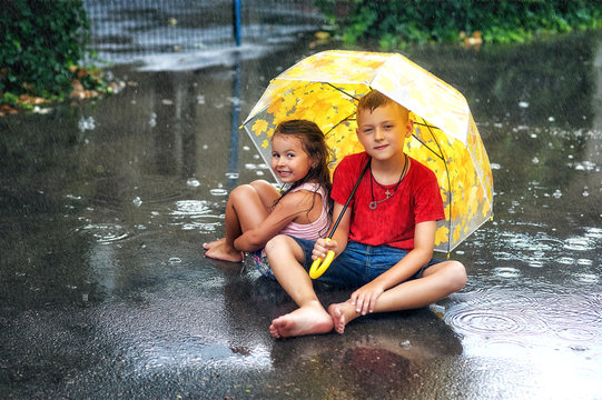Cheerful boy and girl with umbrella during summer rain .Children enjoy the warm rain . Walk in the rain