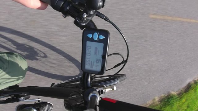 City e bike or electric bicycle  riding in the park track trail at summer. View from first person perspective POV with action camera to the electric speedometer or controller with power level. 4k.