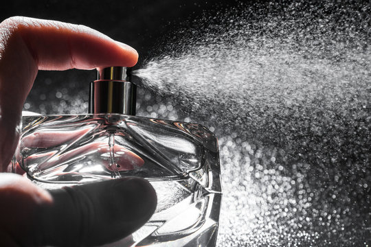spraying perfume on dark background, closeup