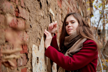 Girl in a red coat near the red brick wall in the Park in late autumn