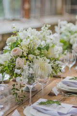 Beautiful composition with bouquets of flowers and candles on a wooden long table near the white plates for guests at a wedding or birthday party