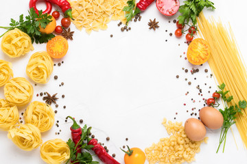 Italian pasta of different kinds with spices, red hot pepper, eggs, yellow and red tomatoes on a white stone background. Concept cooking Italian pasta and sauce. Flat lay, top view. circle shape