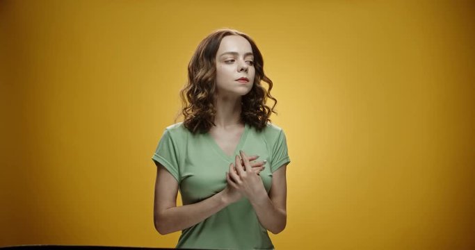 Young female caucasian model looking at camera in temptation, rubbing her palms, isolated on yellow background close up 4k footage