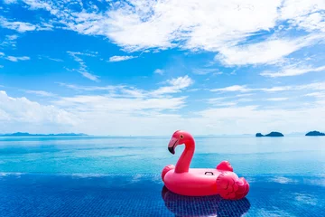 Gardinen Beautiful outdoor swimming pool in hotel resort with flamingo float around sea ocean white cloud on blue sky © siraphol