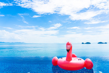 Beautiful outdoor swimming pool in hotel resort with flamingo float around sea ocean white cloud on...