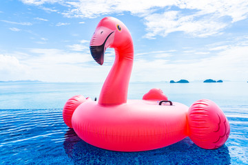 Beautiful outdoor swimming pool in hotel resort with flamingo float around sea ocean white cloud on blue sky © siraphol