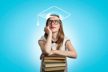 Young girl student leaning on a pile of books and looking up on a blue background. A painted...