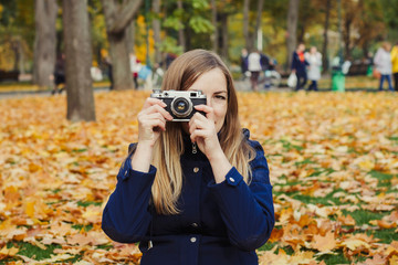 Young pregnant girl holds a camera and takes a picture. Autumn Park. Concept of the onset of autumn and recreation in outdoor
