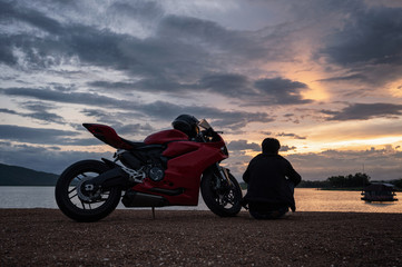 Young biker sitting on side of sport big bike with sightseeing at sunset