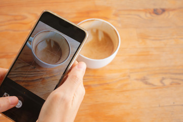 A Woman use cellphone take cup of  hot coffee