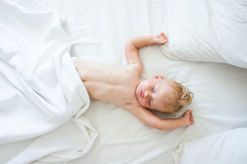 Obraz na płótnie Canvas Baby sleeps in bed with white sheets. The concept of a good and sound baby sleep. Flat lay, top view. Copy space