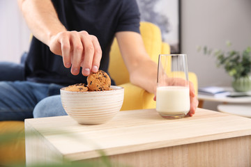 Handsome young man eating tasty cookies with milk at home