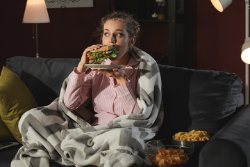 Beautiful young woman eating unhealthy food at night